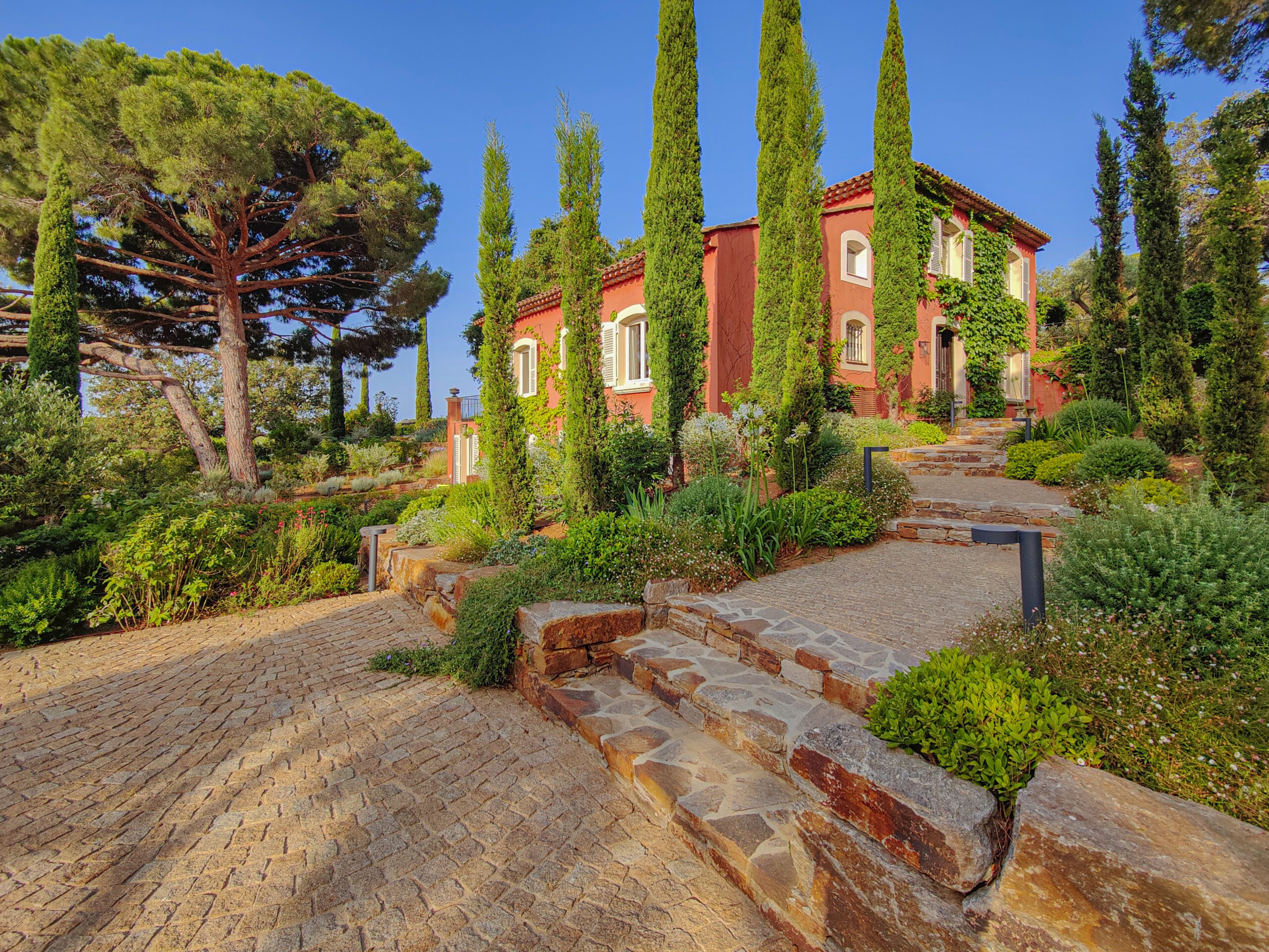 Bastide rose-orangée et cyprès colonnaires Bastide rose-orangée bordée de cyprès colonnaires et allée pavée par MR Paysage